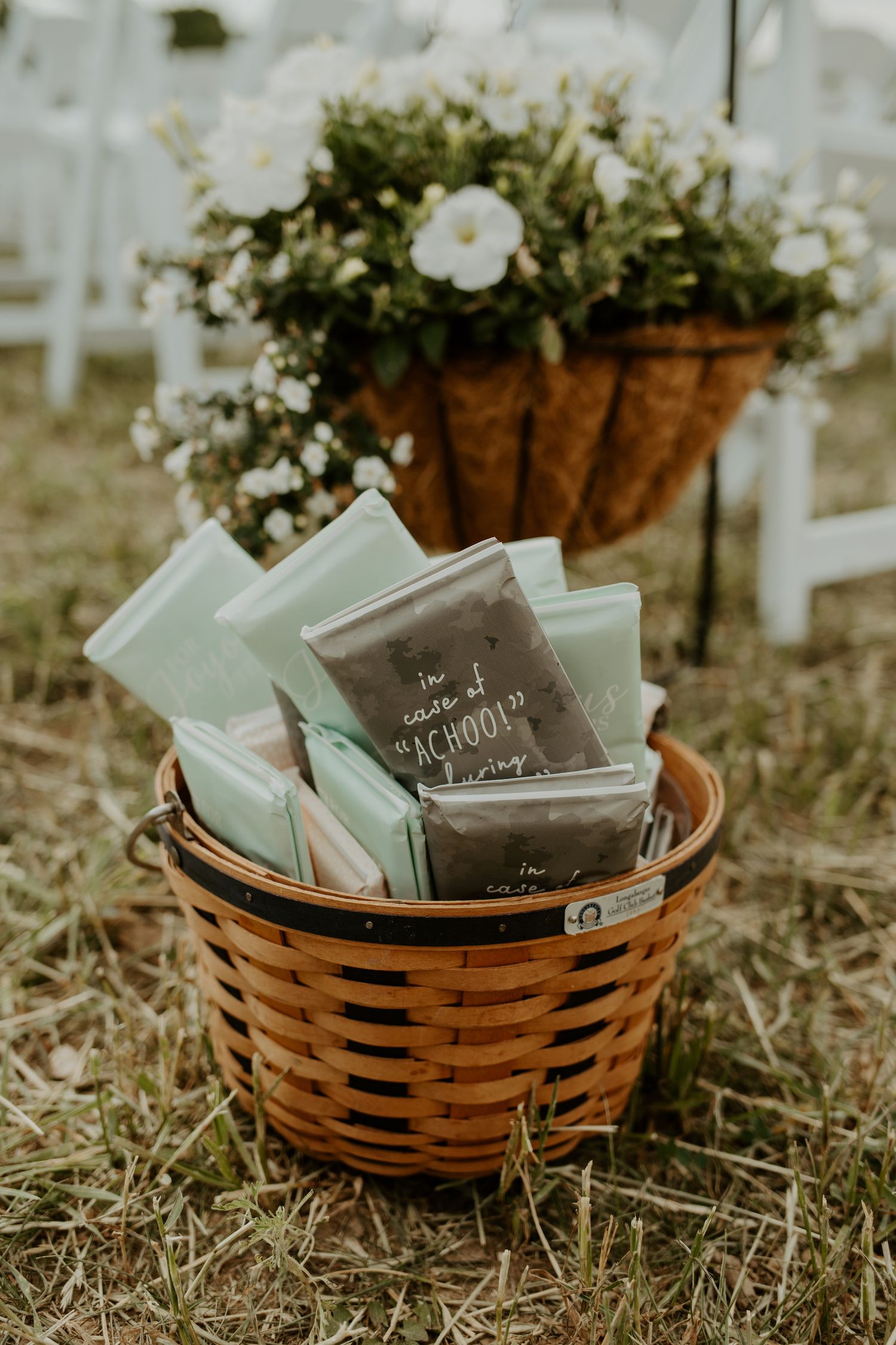 Wedding programs in mint colors arranged in a brown wicker basket with white flowers.