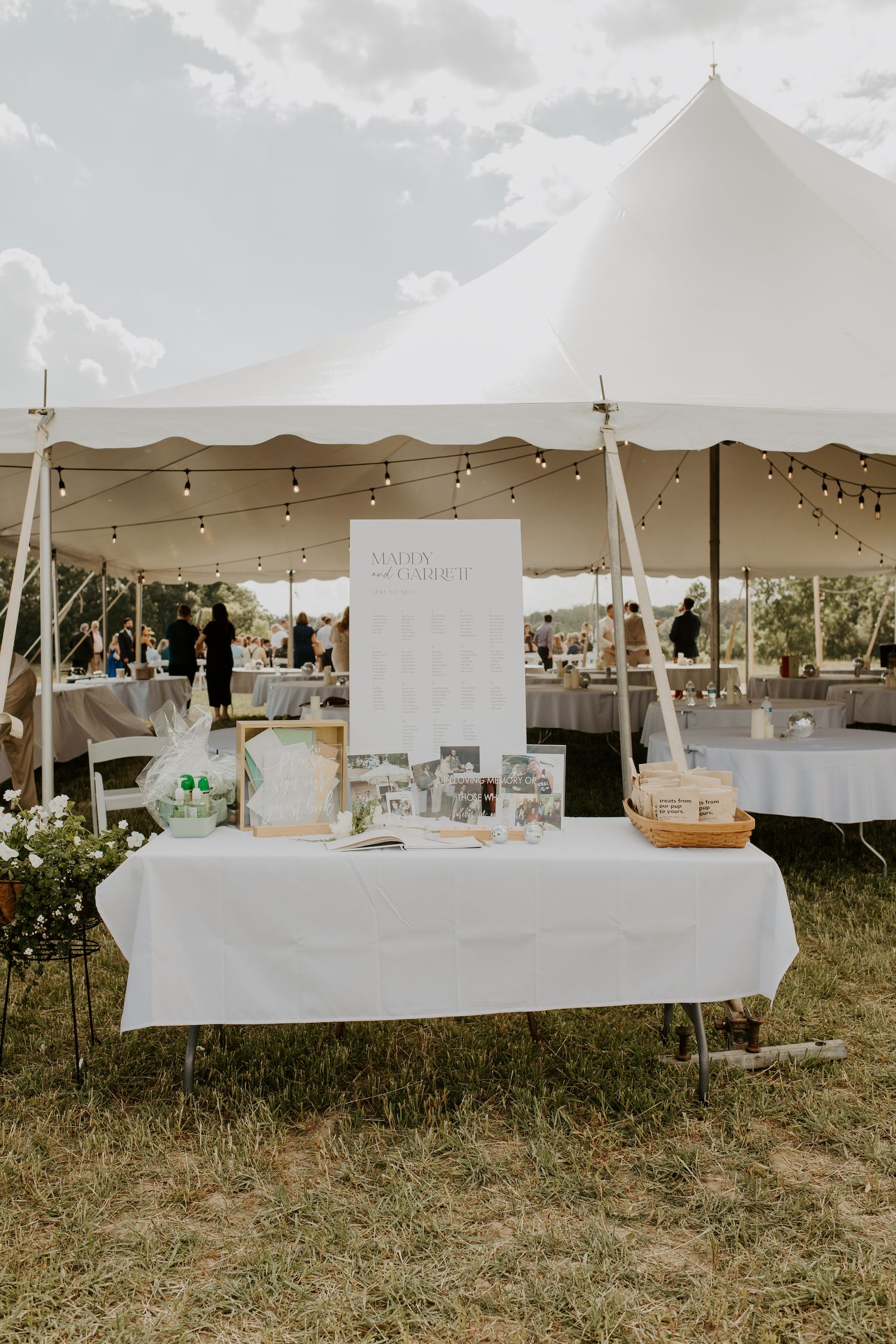 A wedding gift table setup under a white tent with string lights and tablecloths.