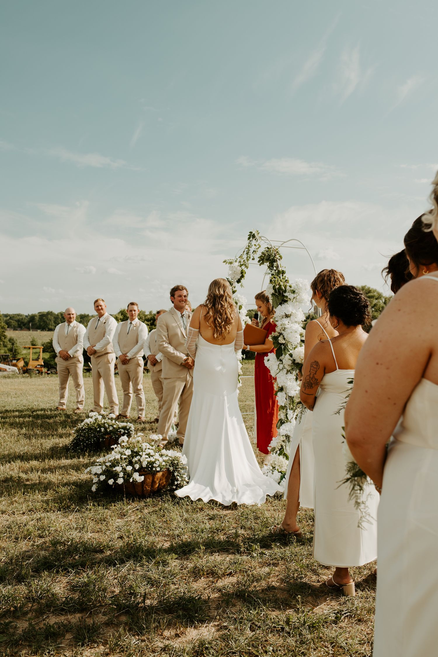 Wedding party lined up during outdoor ceremony with floral arch and greenery.