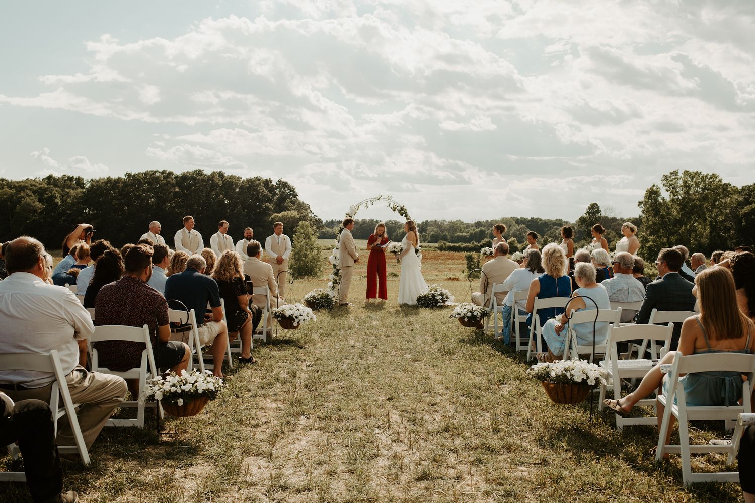 Wide angle view of outdoor wedding ceremony with white chairs and floral decorations.