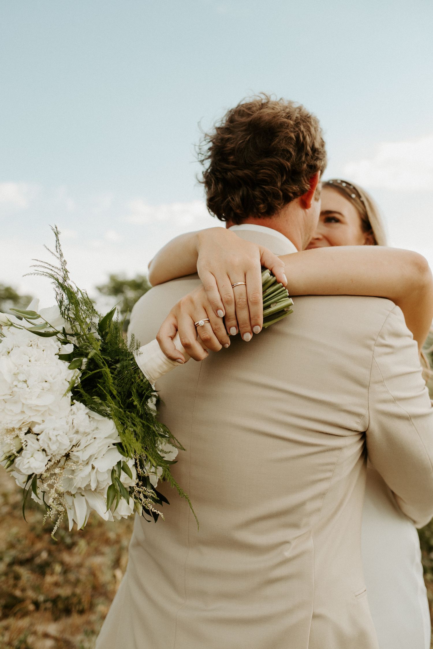 Close-up wedding photo showing an intimate embrace with white bouquet details.