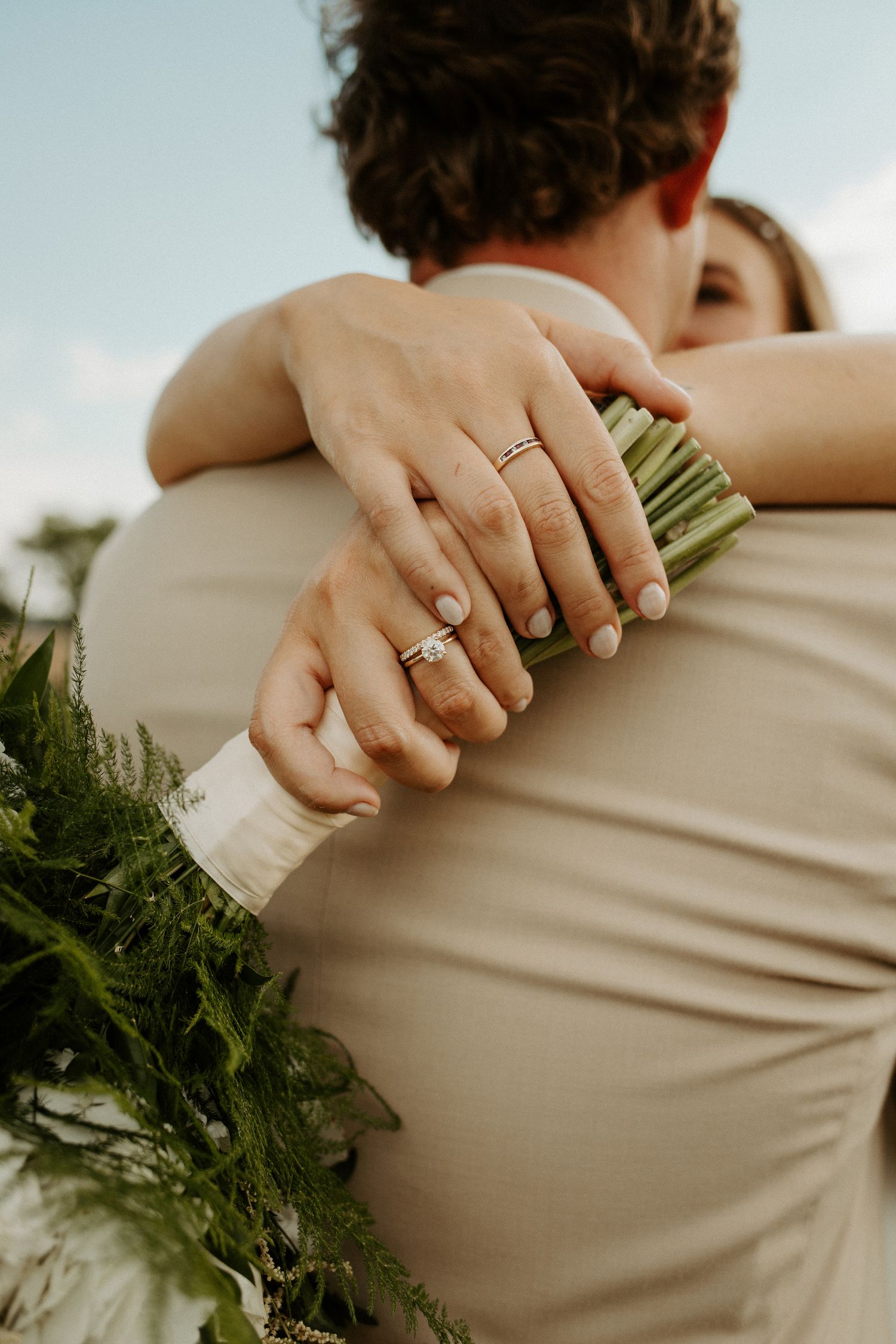 Close-up of hands embracing during wedding moment with rings and floral bouquet visible.