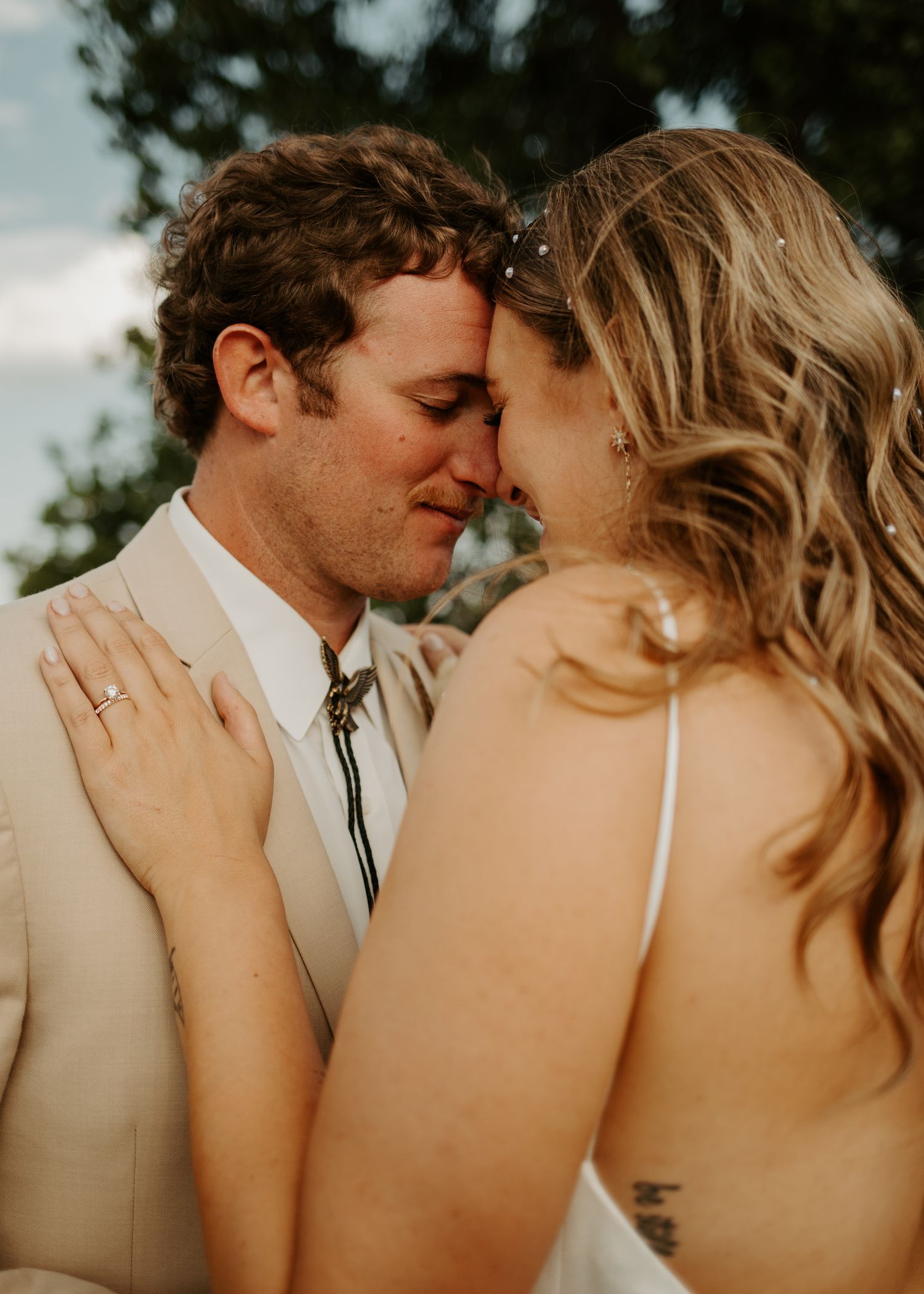 Tender moment between newlyweds in golden sunlight wearing beige and white attire.