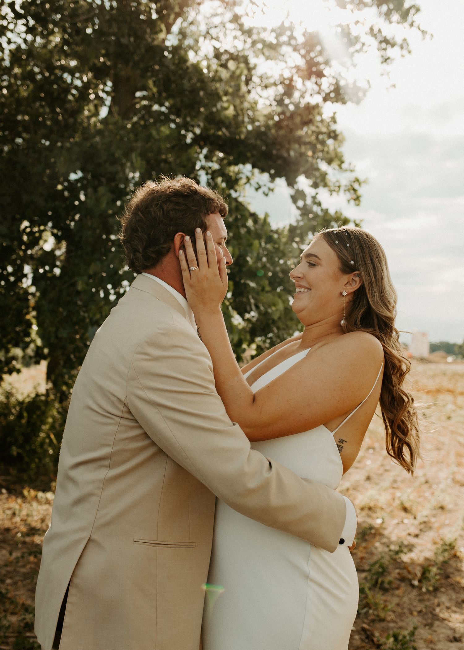 Joyful candid moment between newlyweds touching faces and laughing outdoors.