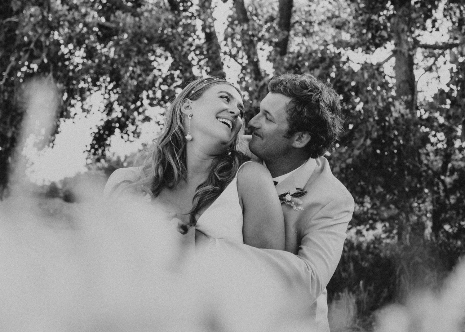 A black and white wedding portrait capturing a joyful intimate moment between newlyweds.