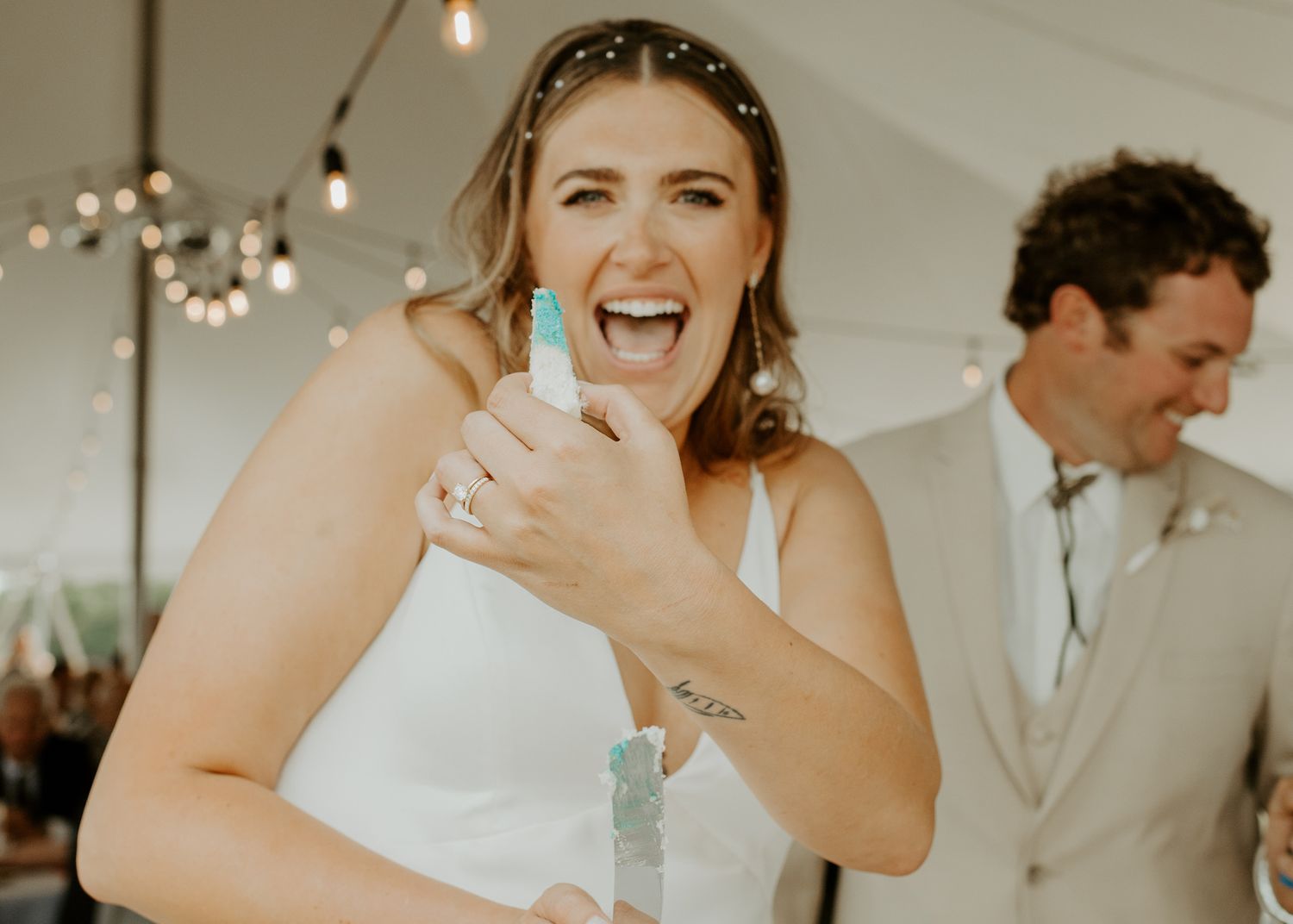 A reception photo of a happy couple celebrating under a white tent with string lights.