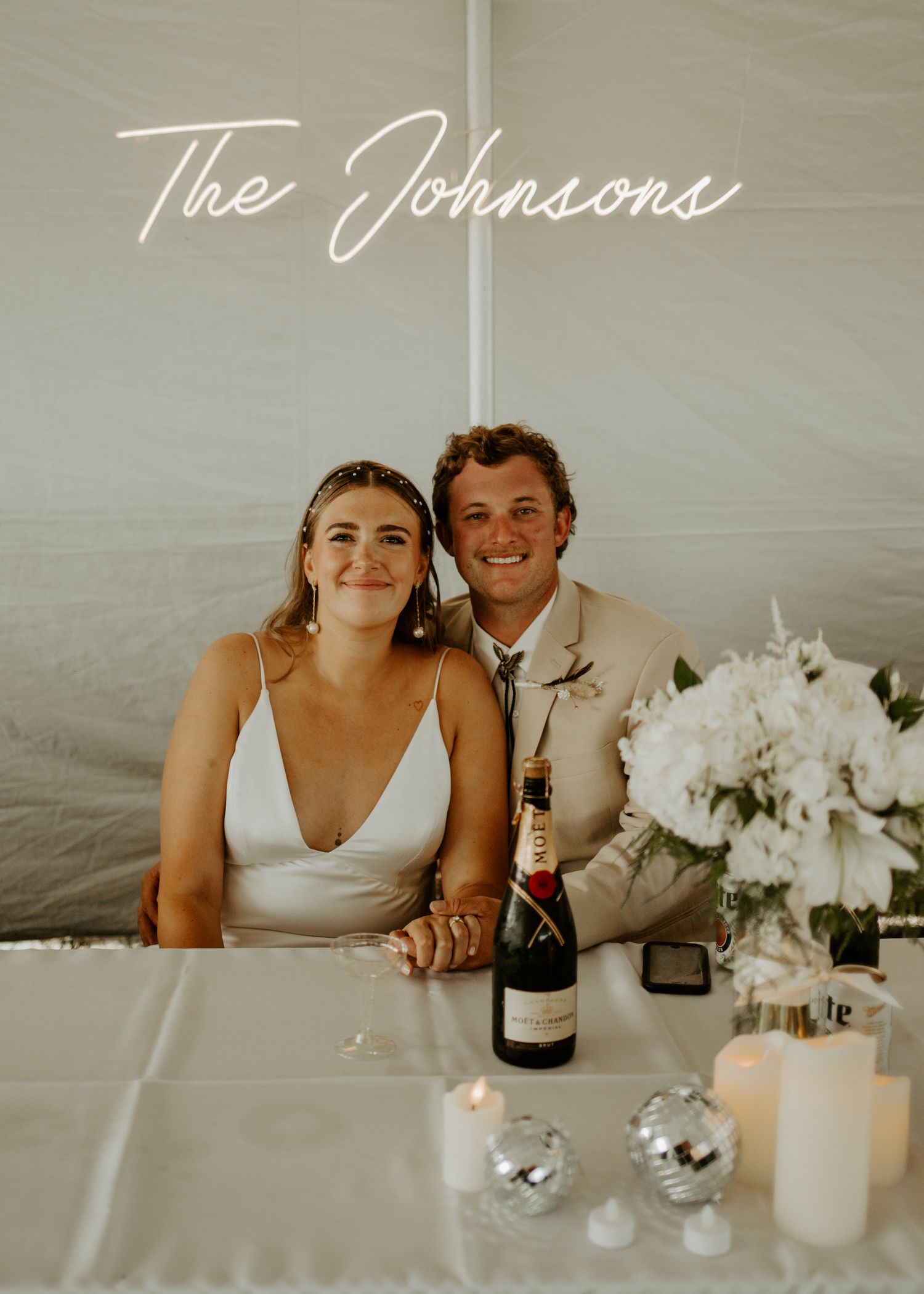 A couple sits at their wedding reception table with champagne and elegant white floral decorations.