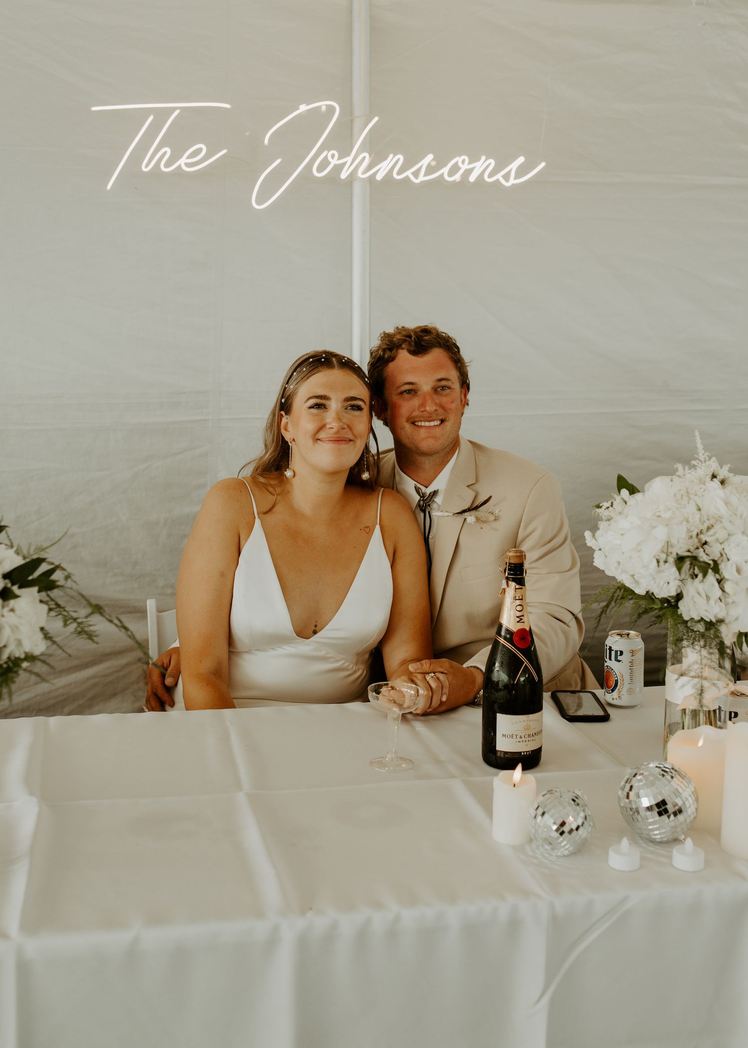Reception table scene with newlyweds and champagne under elegant script signage.