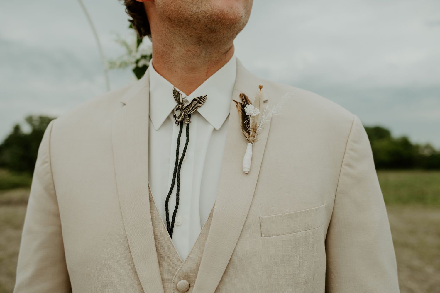 Close-up detail of a beige wedding suit with a bolo tie and boutonniere.