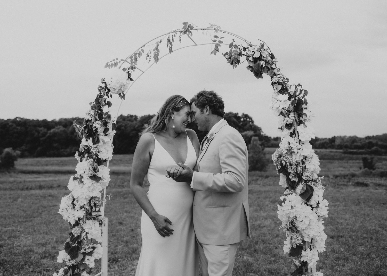 Wedding couple sharing intimate moment under floral arch in black and white.