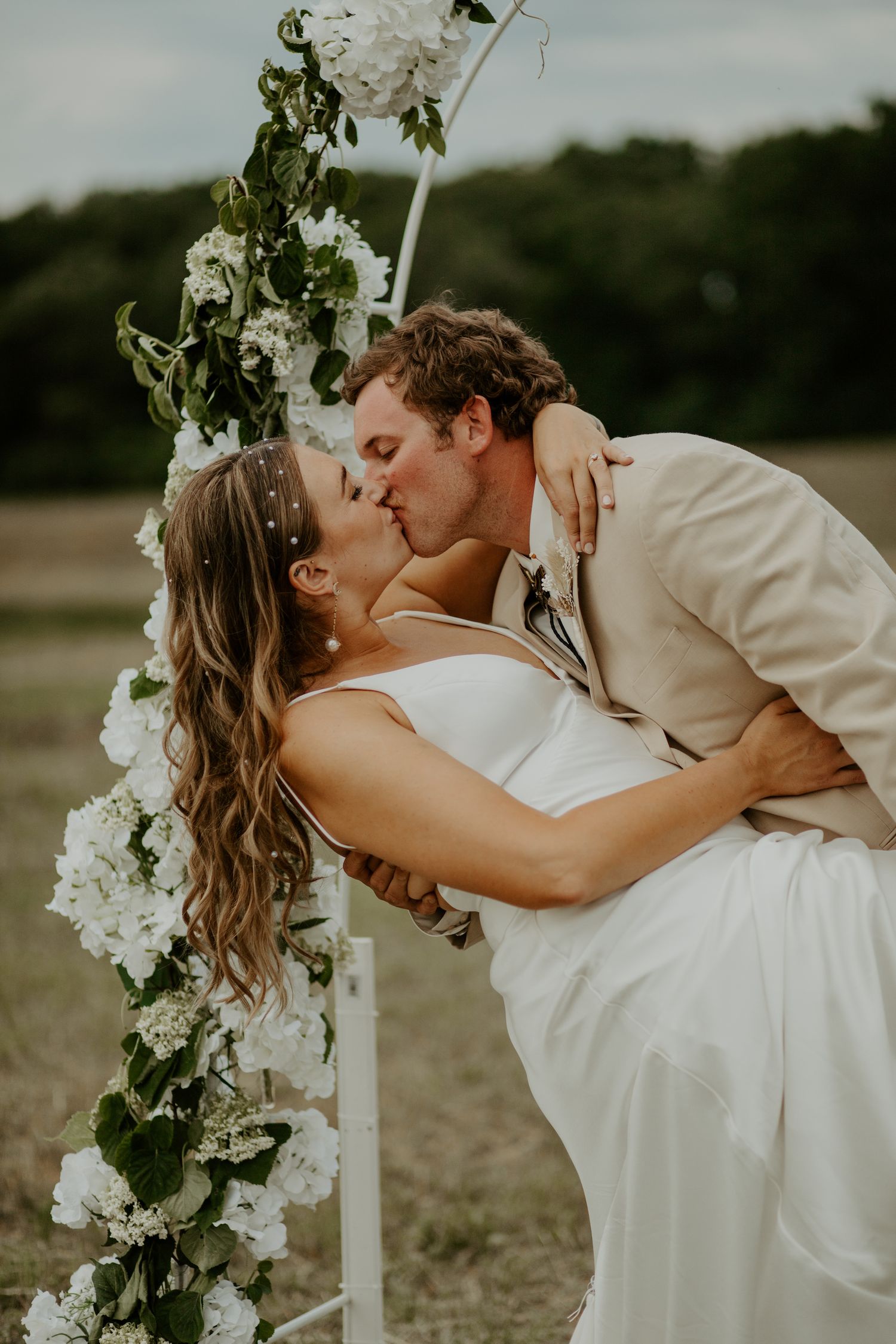 Romantic kiss by floral-decorated arch during outdoor wedding ceremony.