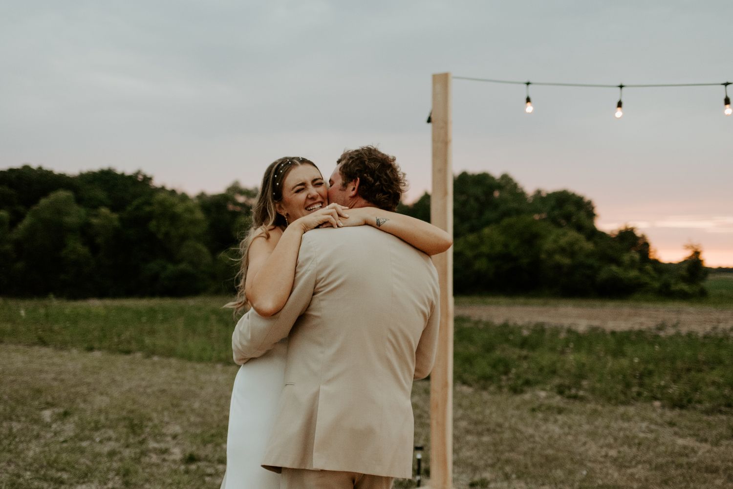 Tender embrace during sunset at outdoor wedding reception.