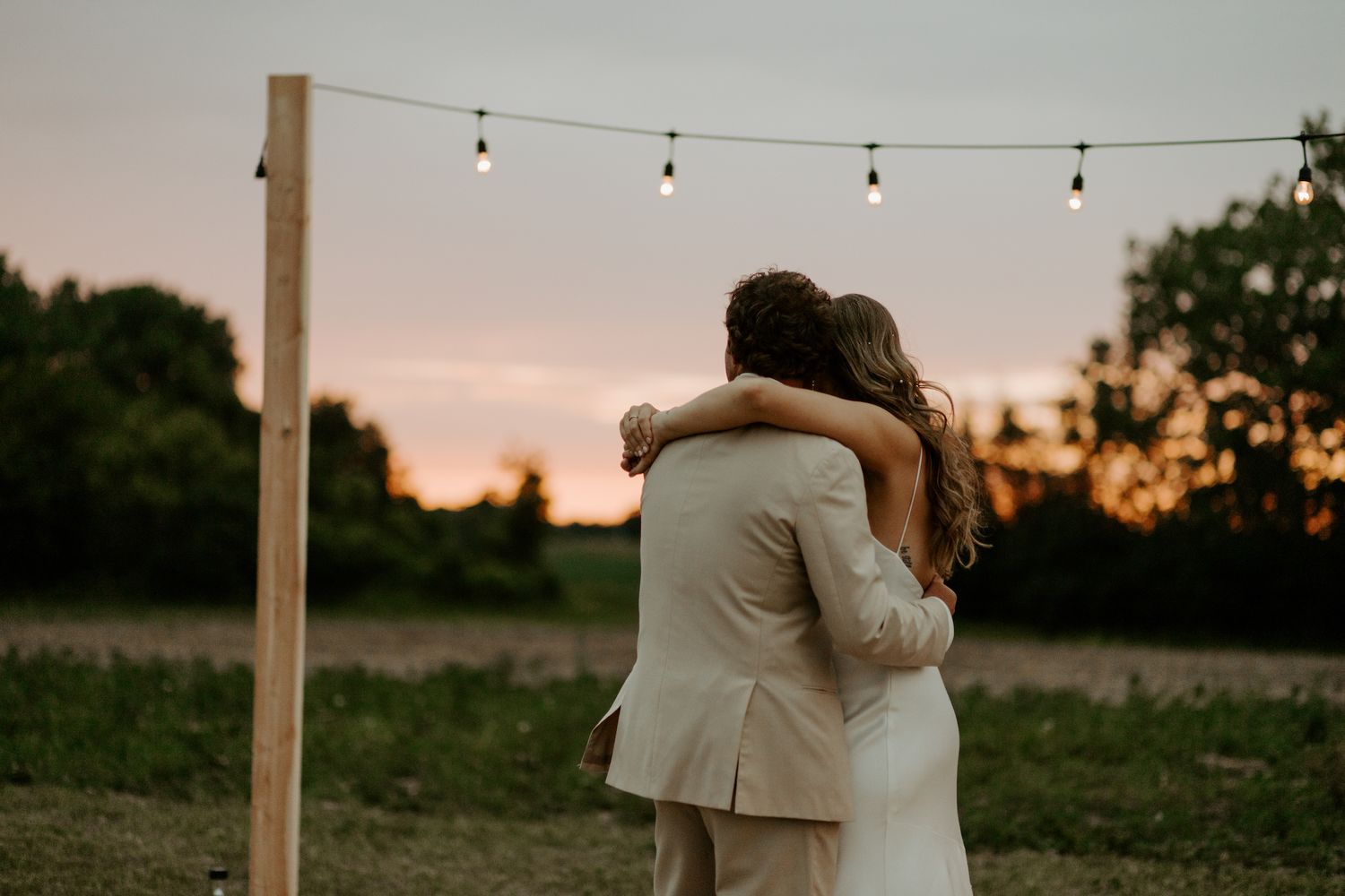 Couple embraces during sunset under string lights on an outdoor wooden platform.