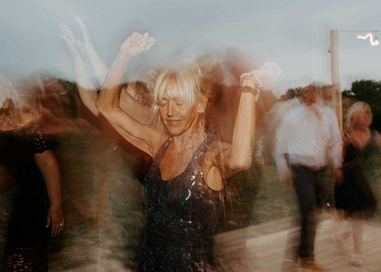 Motion-blurred image captures energetic dancing at an outdoor evening celebration.