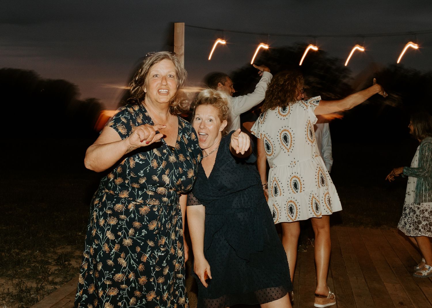 Joyful guests dancing and celebrating at an outdoor evening event under string lights.