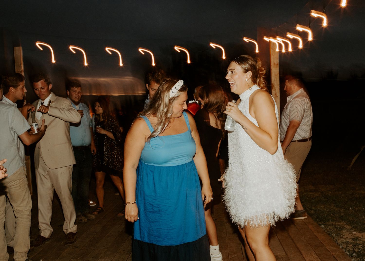 Friends dancing together at an outdoor evening celebration under warm string lights.