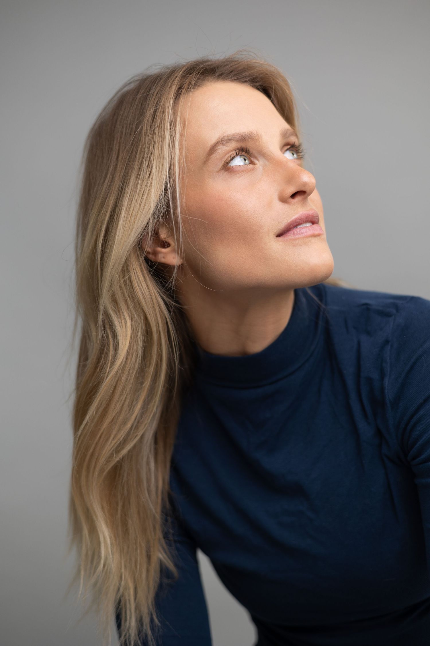 Profile portrait of person in navy top looking upward against light grey background.