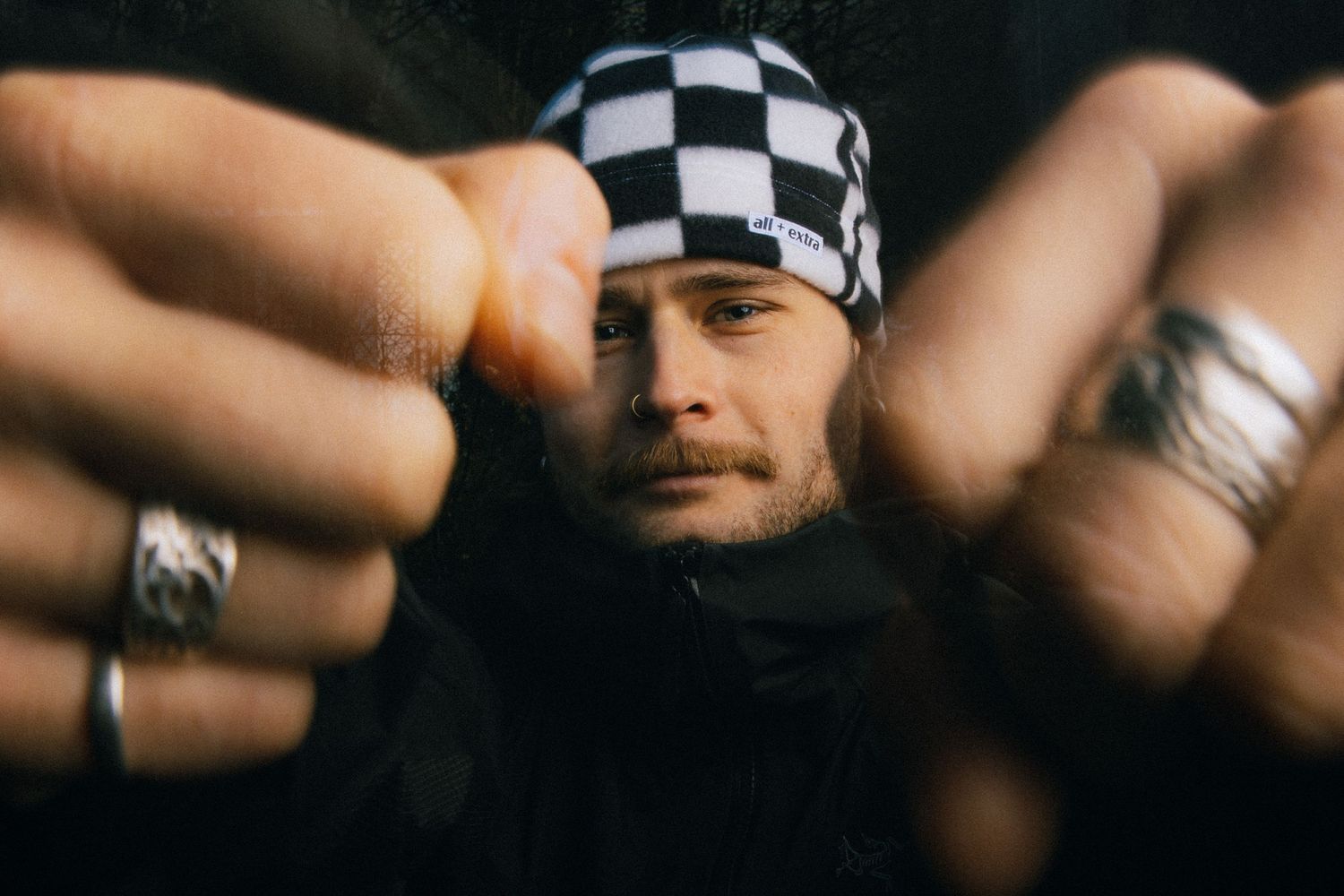 Person wearing a black and white checkered beanie and rings shown in close-up detail.