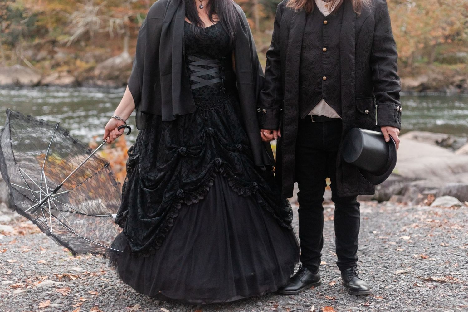 A group dressed in black Victorian gothic attire poses together by a rocky shoreline.