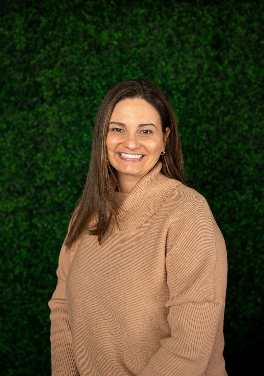 Portrait of professional in beige sweater against green foliage background.