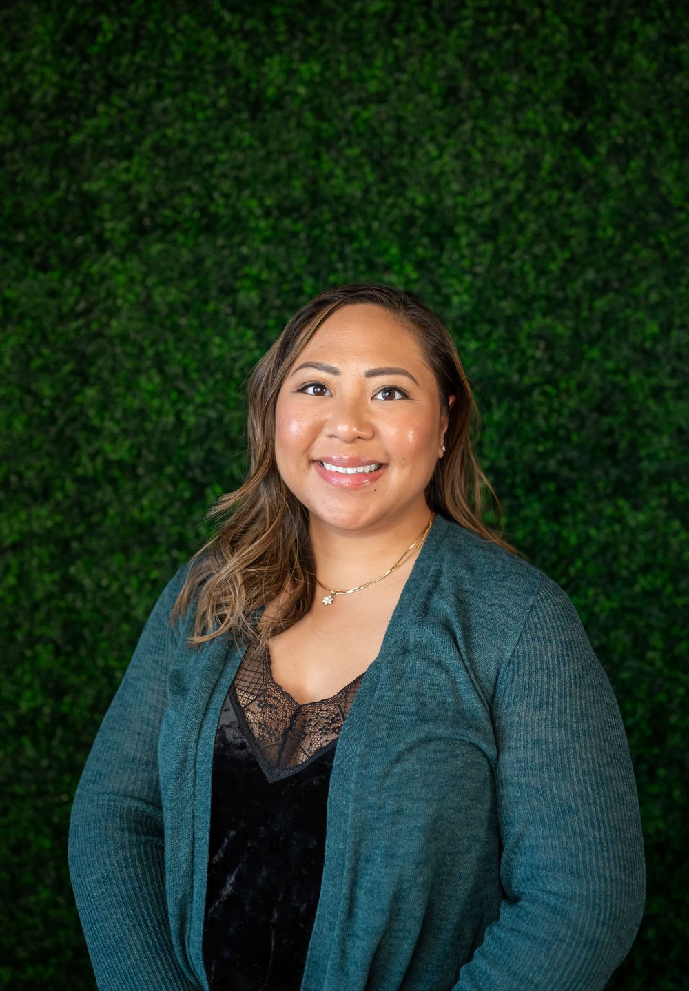 Professional headshot with teal cardigan and lace top against green wall background.