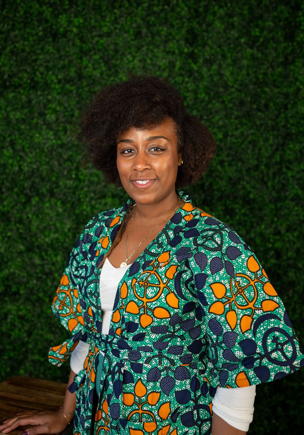 Portrait showcasing vibrant African print dress against lush green backdrop.