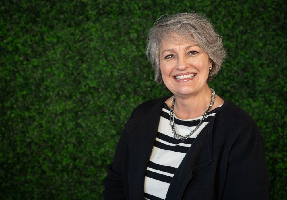 Professional portrait with striped top and black cardigan against green foliage background.