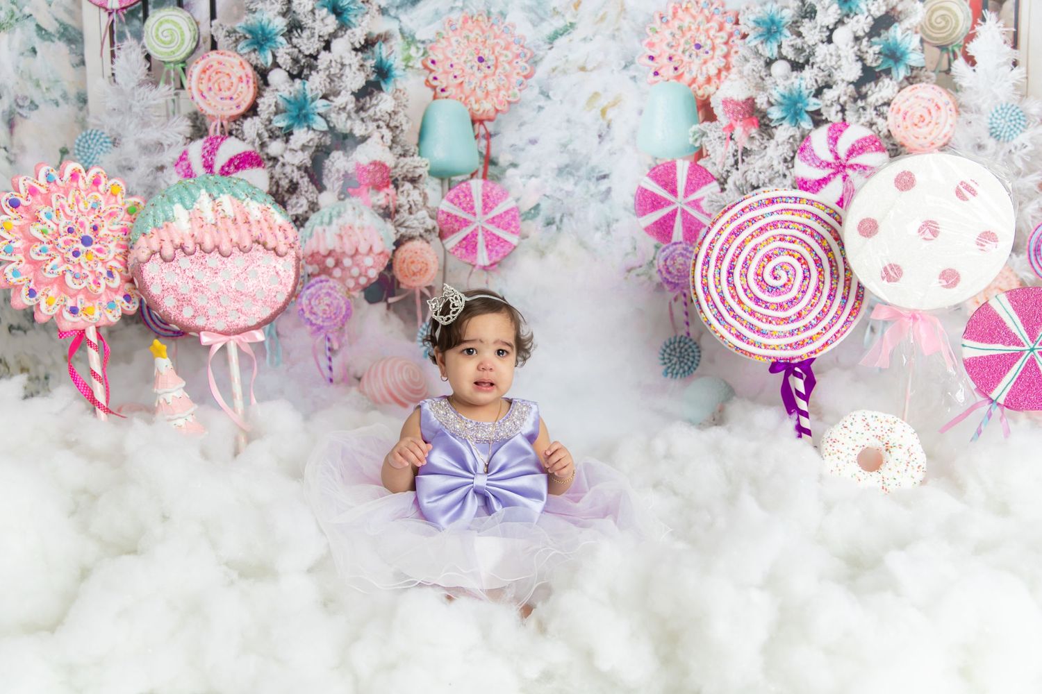 Whimsical winter wonderland photography setup with pink and purple candy-themed decorations and cotton cloud floor.