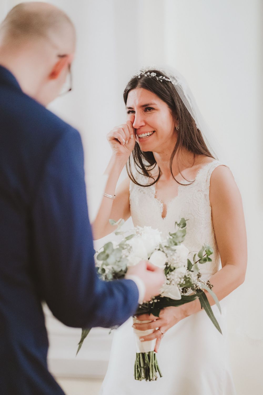 Joyful bride holding white bouquet during indoor wedding ceremony.