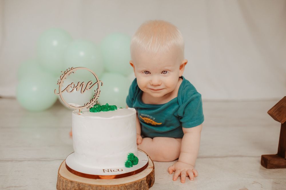 Baby's first birthday celebration with mint green balloons and white cake.