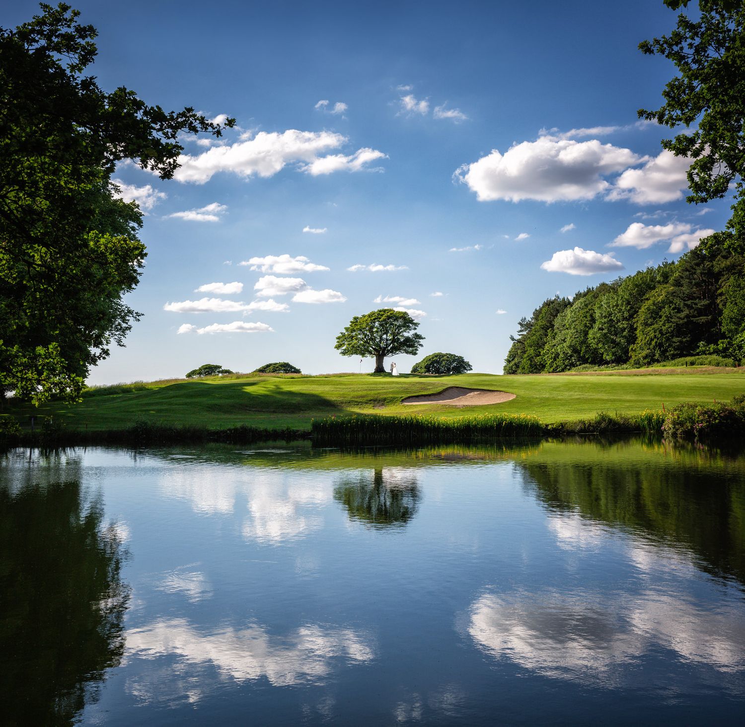 A scenic view at Shrigley Hall wedding venue in Cheshire of bride and groom on the golf course before a large lake