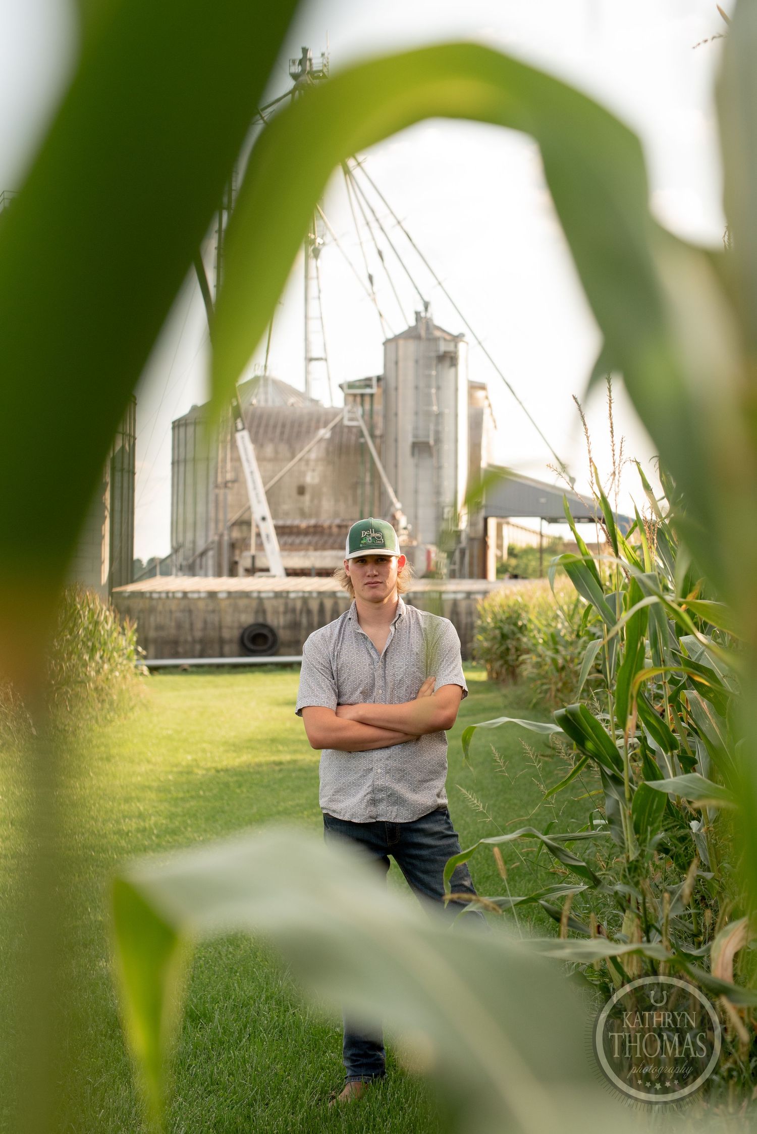 View through corn stalks of grain storage facilities and silos on farm property.