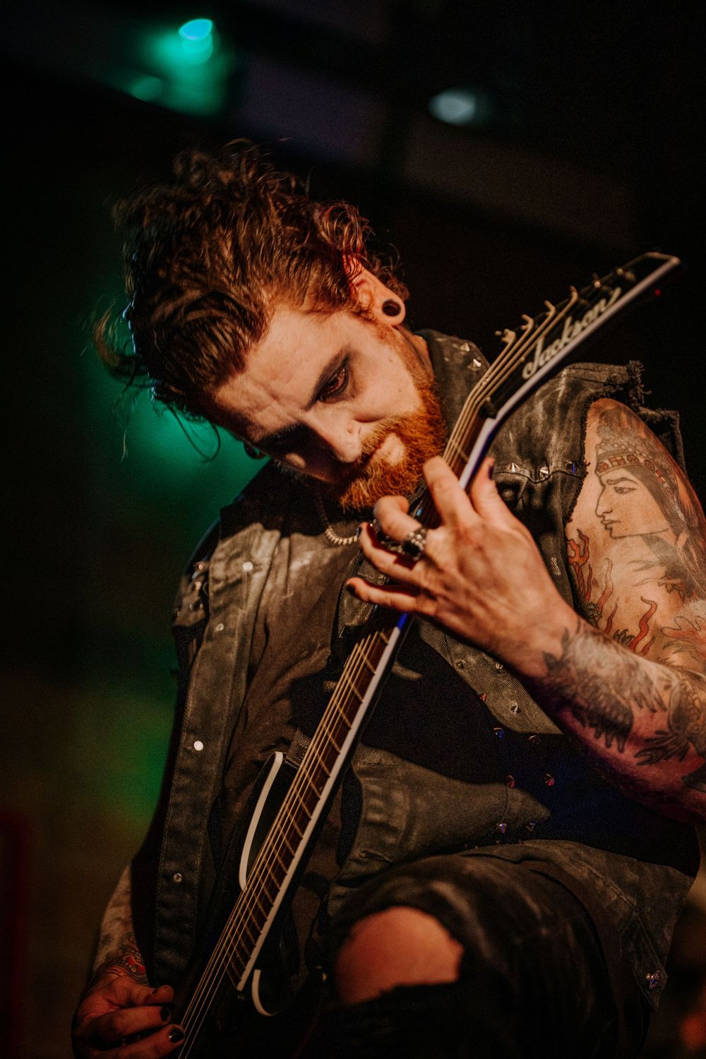 Guitarist with red beard playing passionately during a rock performance.