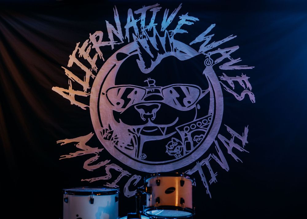 Alternative Lives band logo illuminated against dark backdrop at a concert venue.
