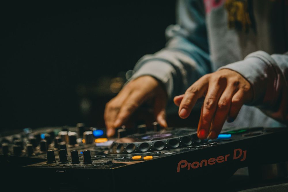 Close-up of hands adjusting controls on a Pioneer DJ mixer in low light.
