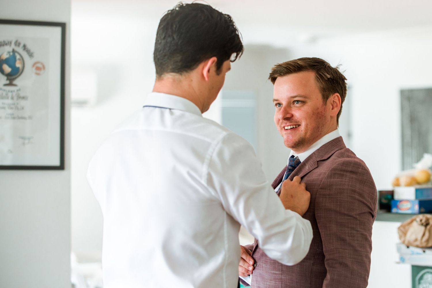 Two people adjusting formal attire and tie before a special event.