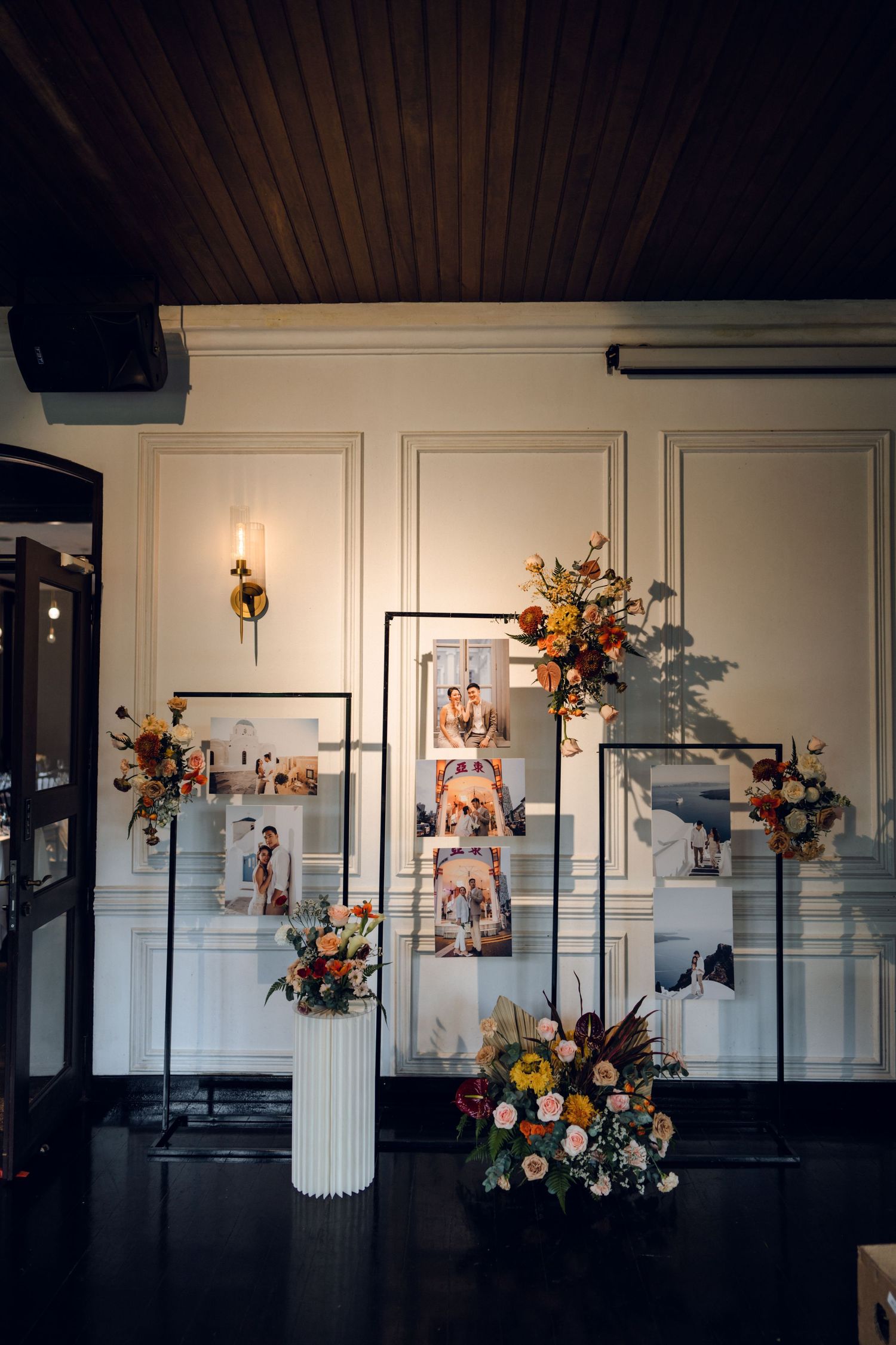 Gallery wall display with white paneling and floral arrangements in a dark-lit event space.