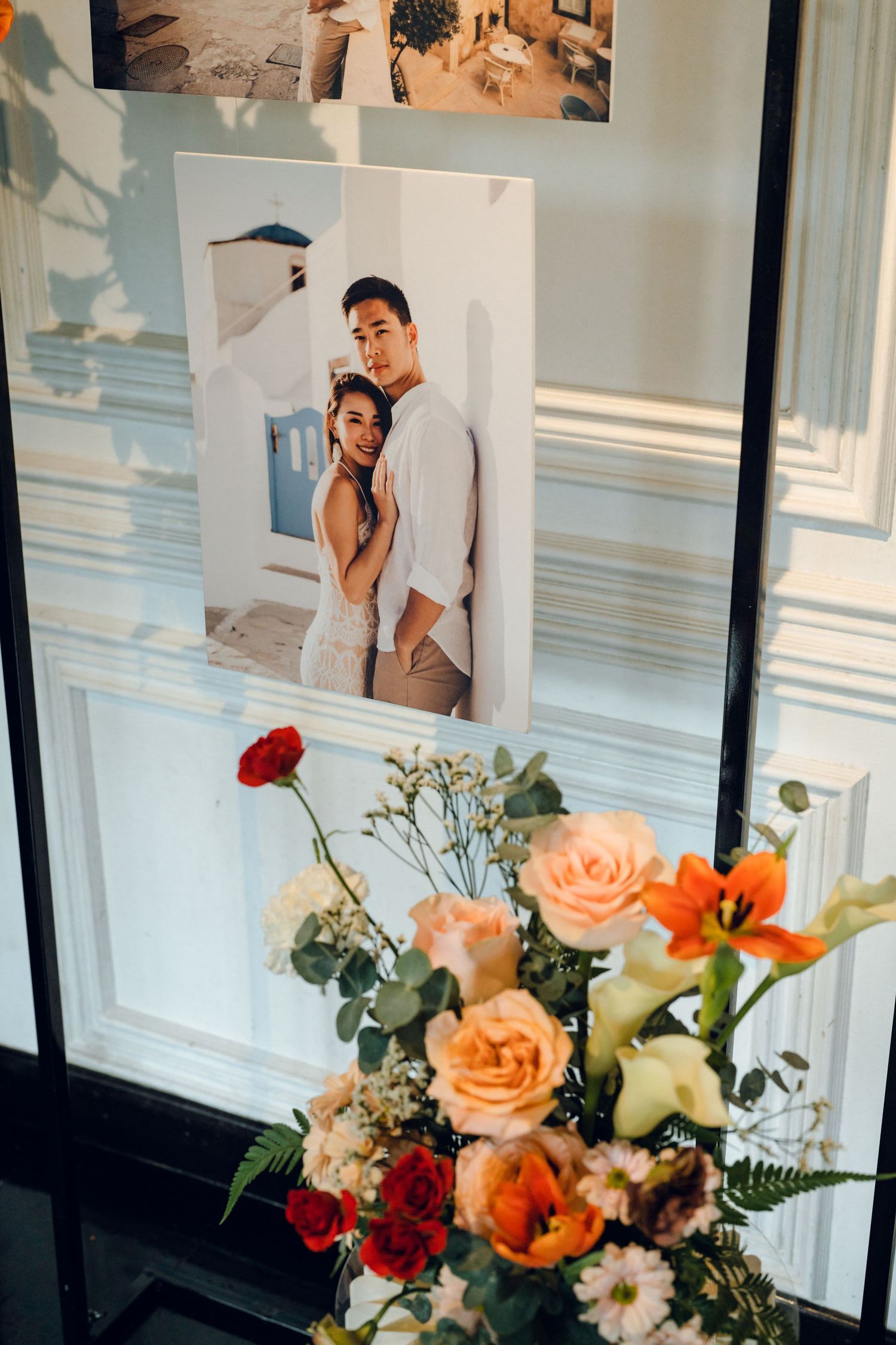 Wedding photo display with peach and orange floral arrangements against white paneled walls.