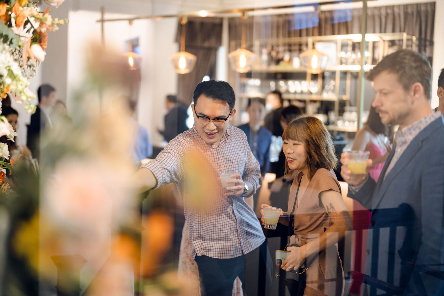 Reception venue with guests gathered near a bar area under warm lighting.