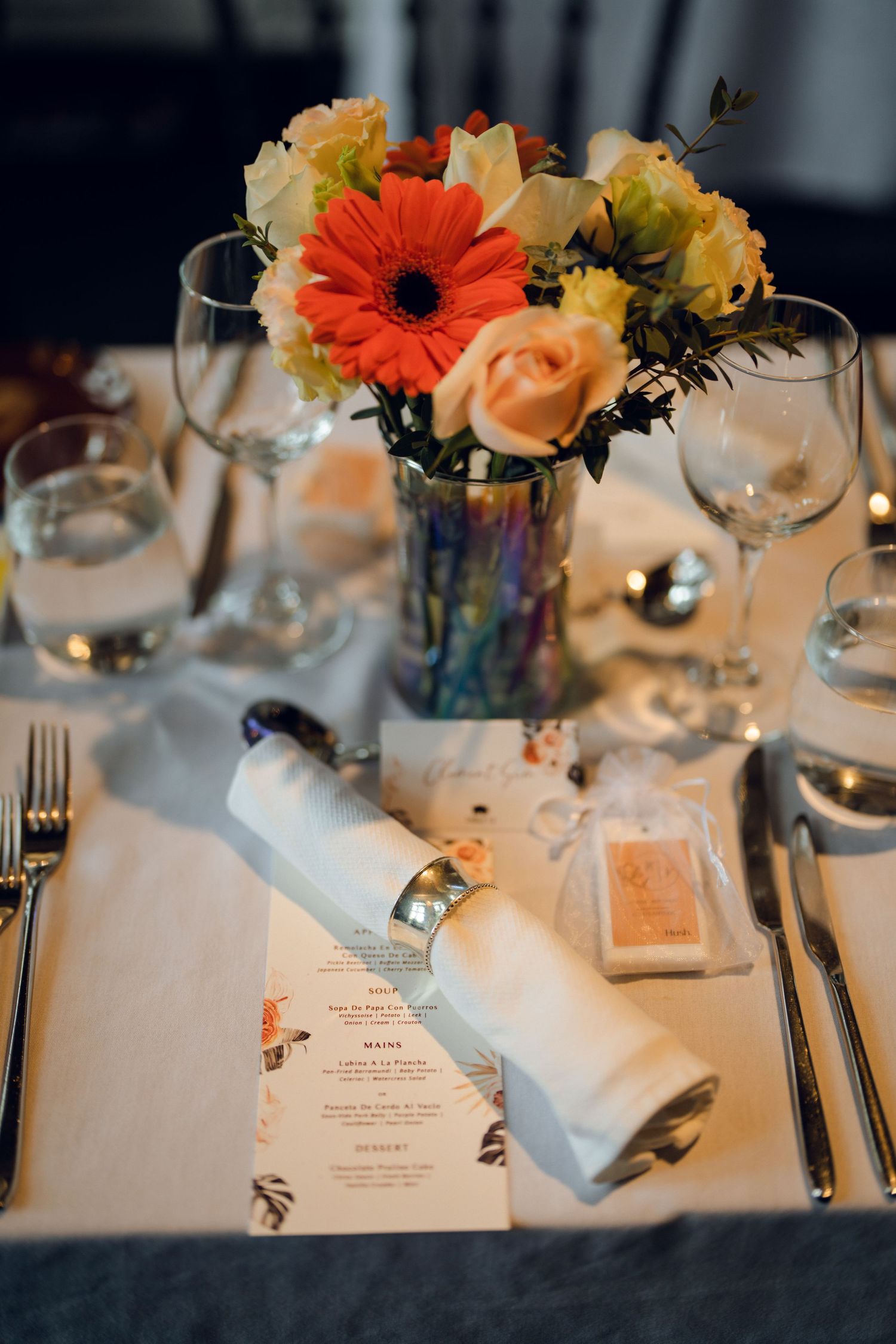 Wedding reception table setting with orange and peach floral centerpieces and elegant place settings.