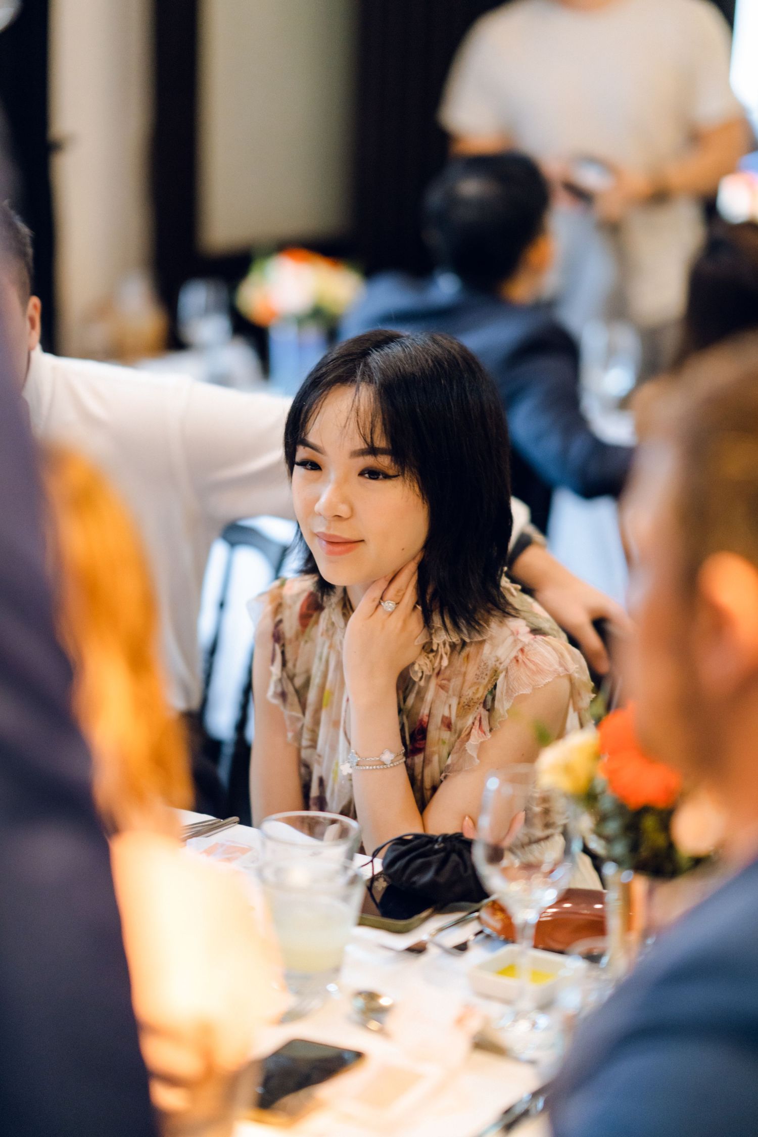 Diners engaged in lively conversation at an elegant restaurant table with floral centerpieces.