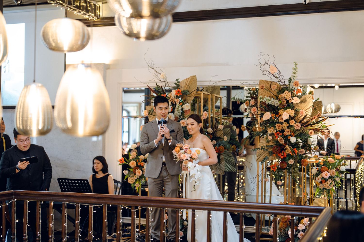 Elegant wedding reception venue with hanging lights and floral arrangements on wooden beams.