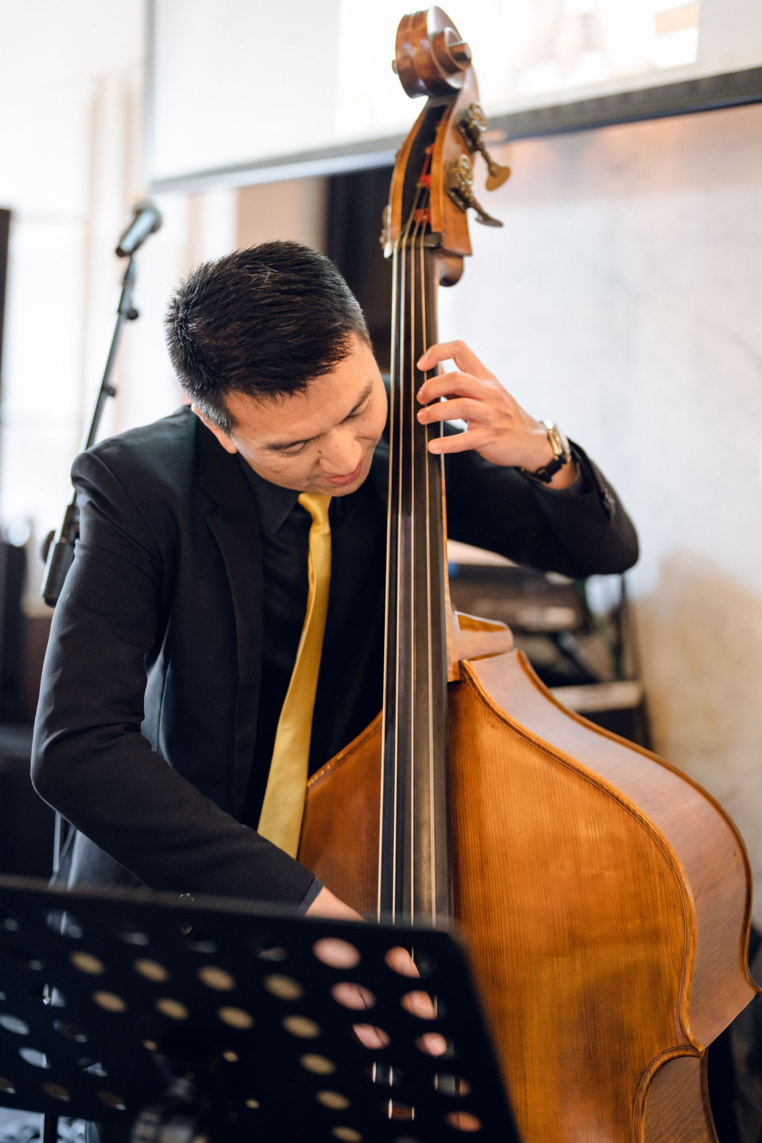 Bass player in formal attire performs on upright double bass at event.