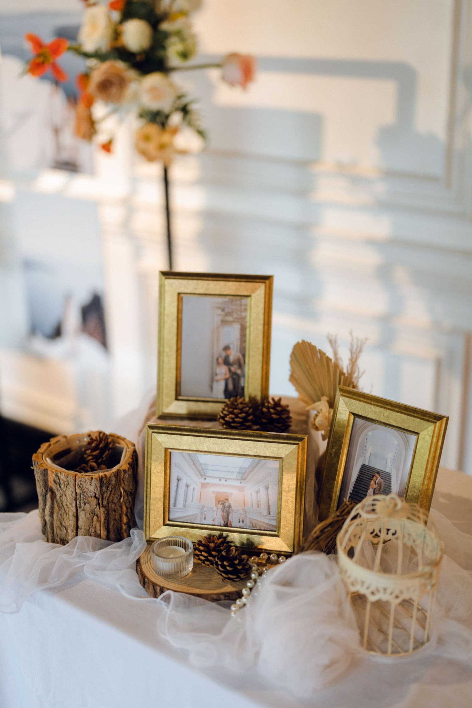 Wedding decor display featuring gold frames, pinecones, and floral arrangements on white tablecloth.