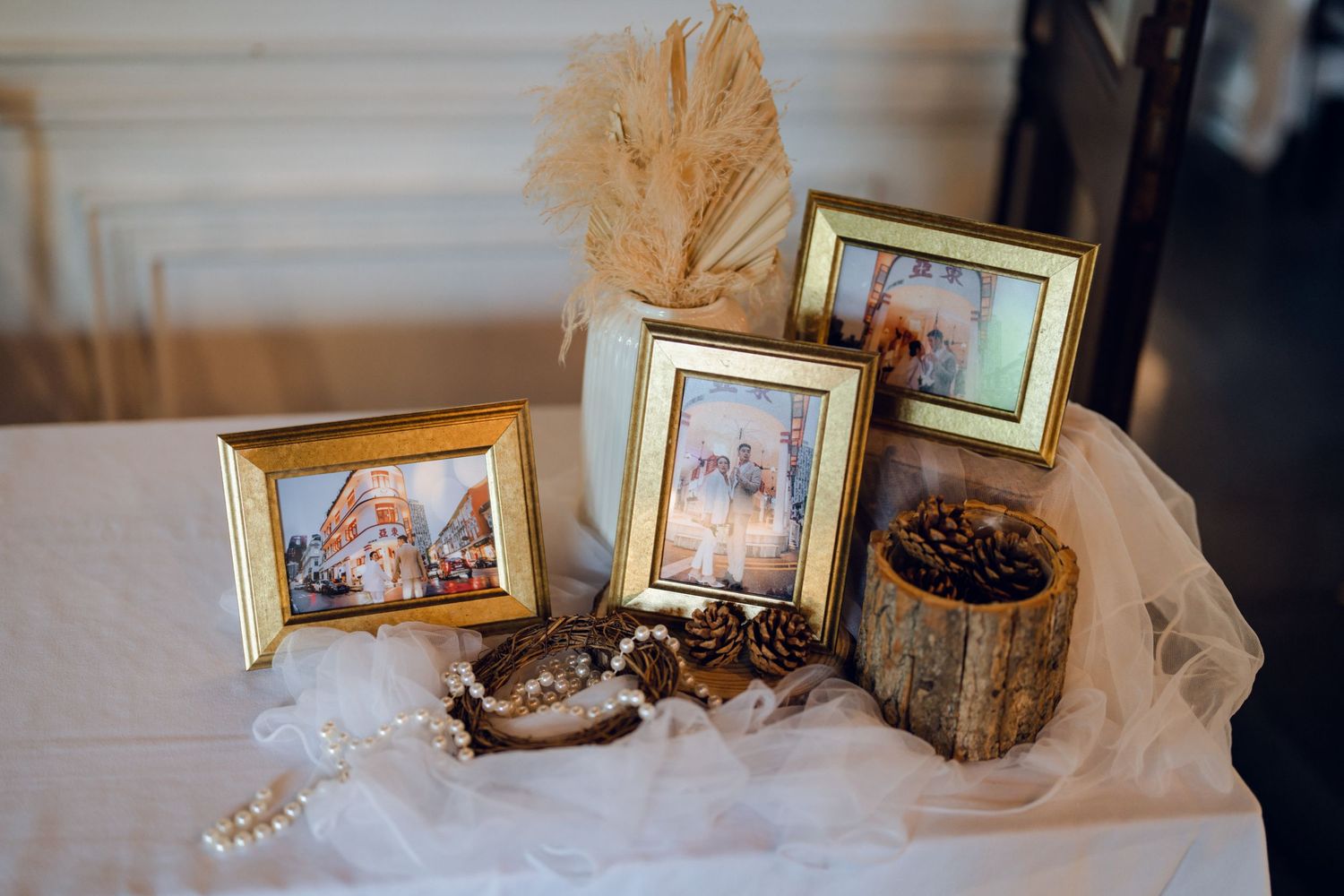 Wedding photo display with gold frames and decorative elements on white table setting.