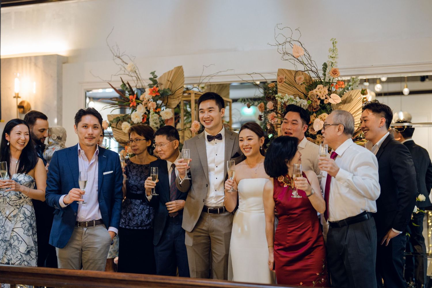 Wedding celebration with guests raising their hands in joy at an indoor venue with floral decorations.