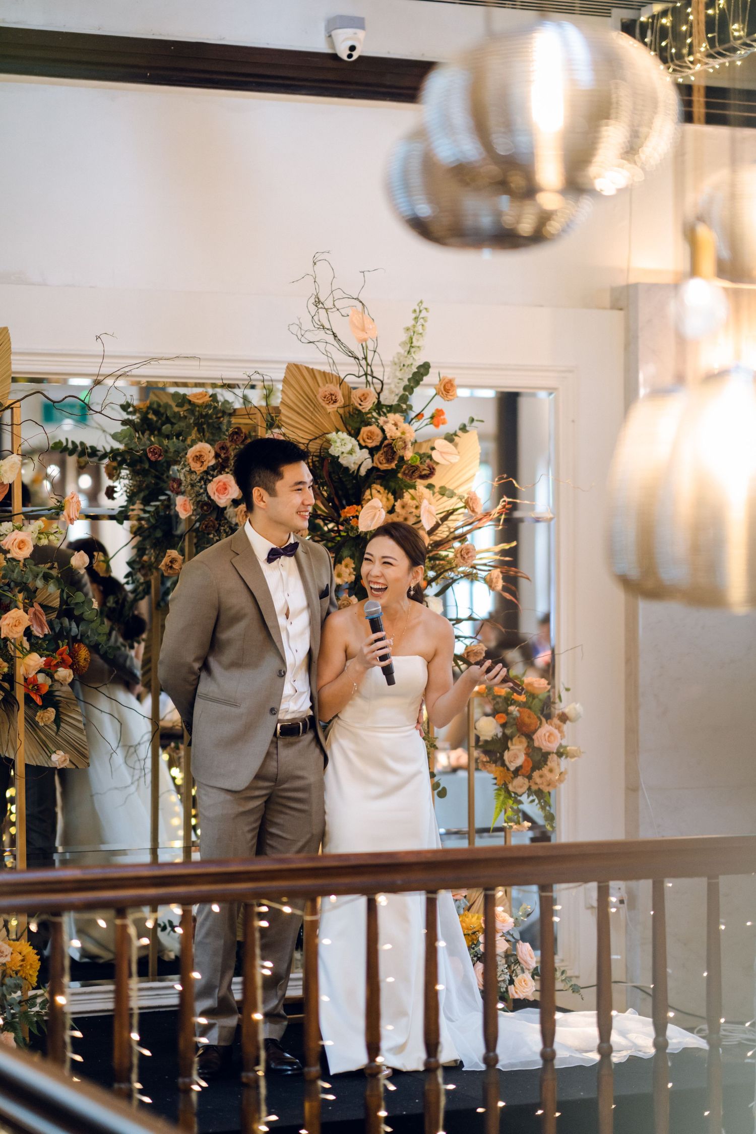 Wedding celebration in a modern venue with string lights and peach-colored floral arrangements.