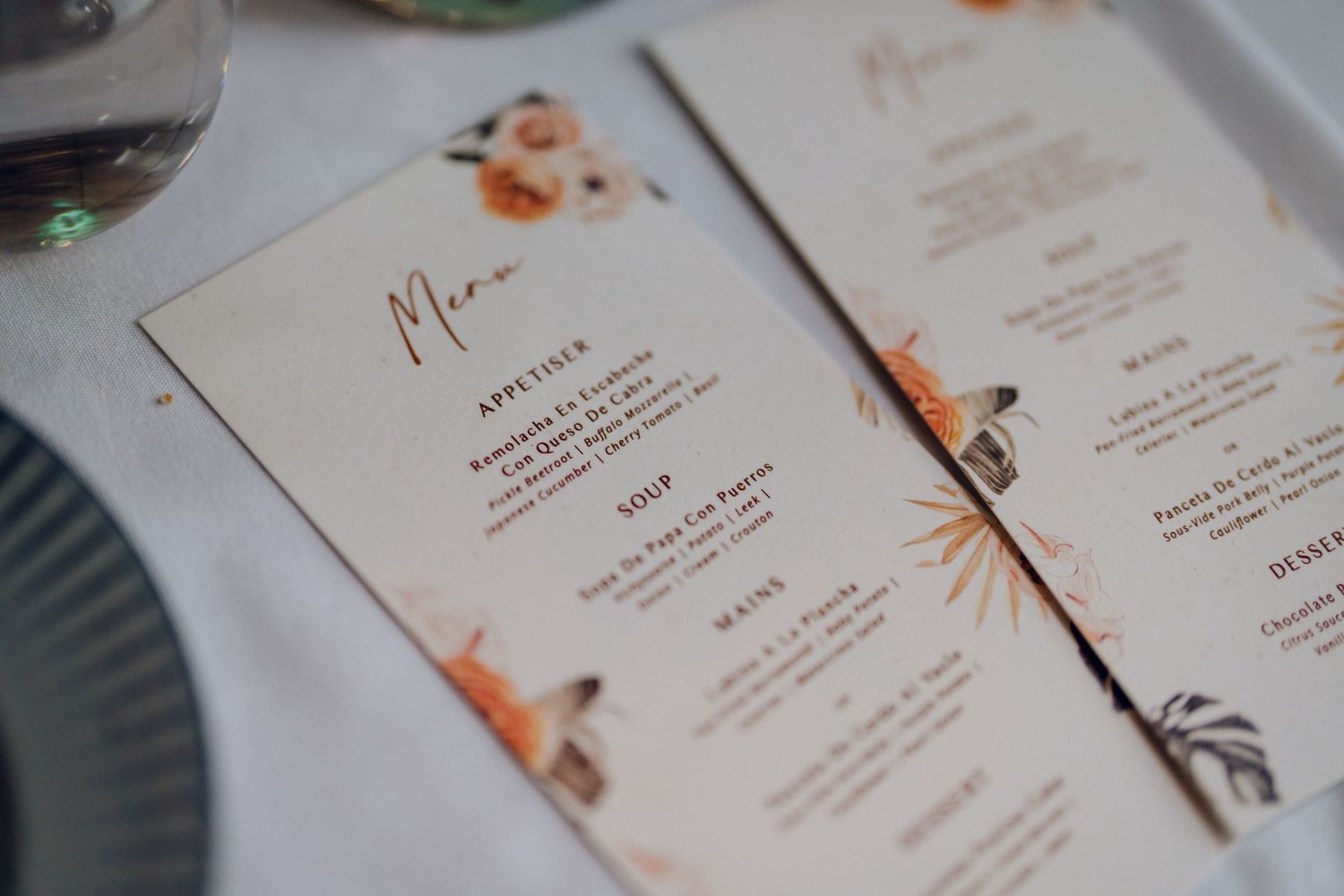 Wedding menu cards with elegant typography and orange watercolor details on white paper.