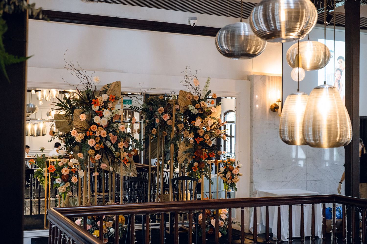 Wedding reception space decorated with hanging metallic pendant lights and floral arrangements.