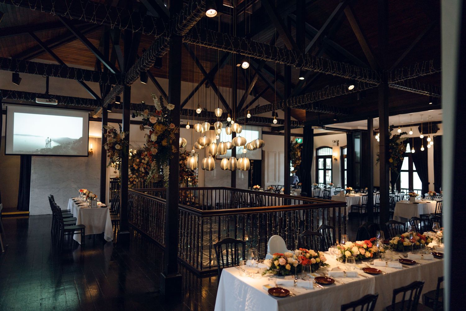 Dimly lit wedding reception venue features rustic beams and elegant chandeliers.